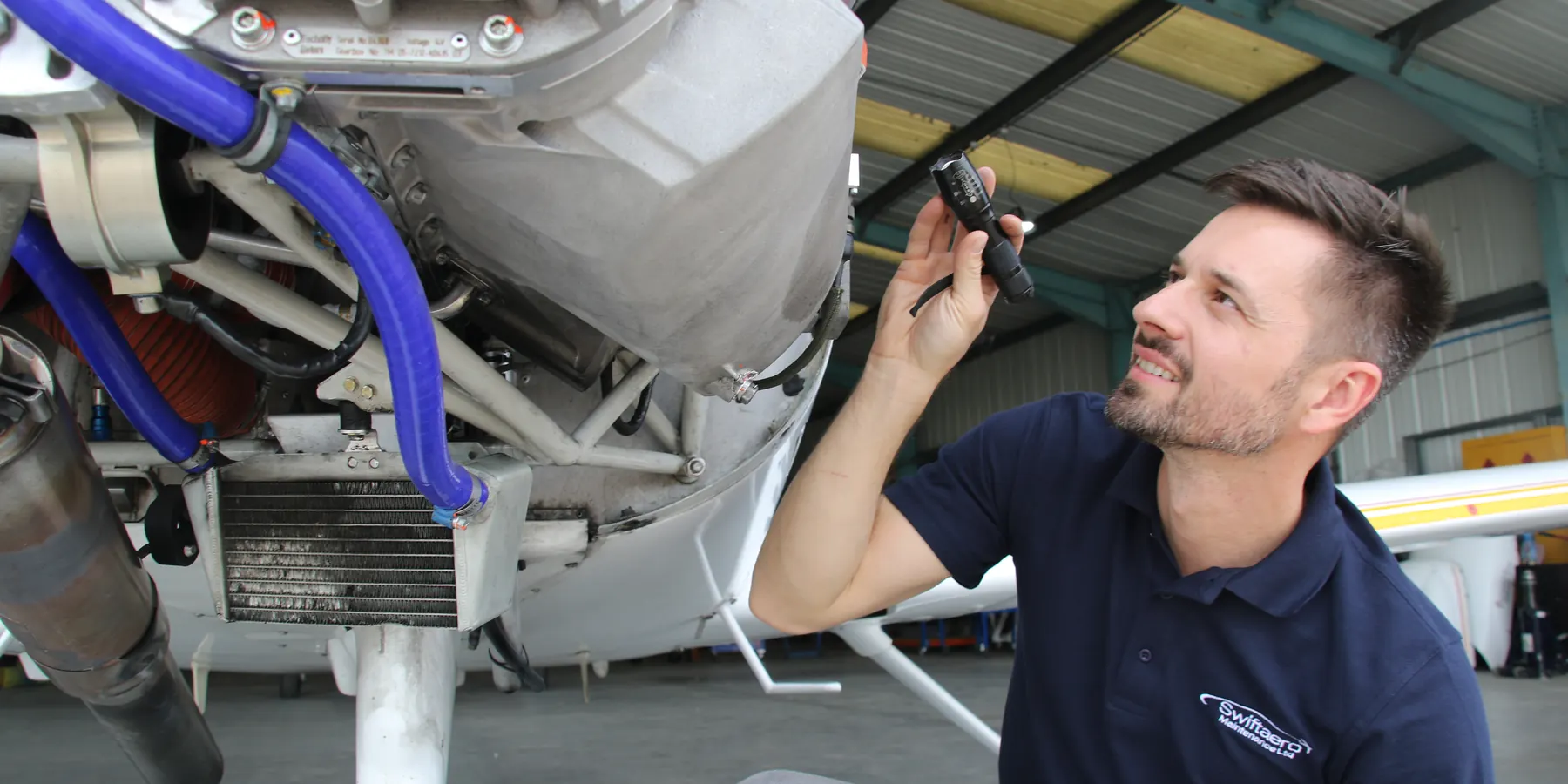 Swift Aero engineer working under the open engine cowling of a light aircraft in the hangar at Sywell Aerodrome